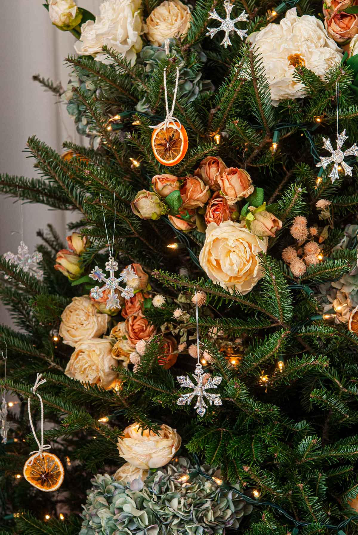 A Christmas tree decorated with lights, fake flowers, orange slices and glass snow flakes.