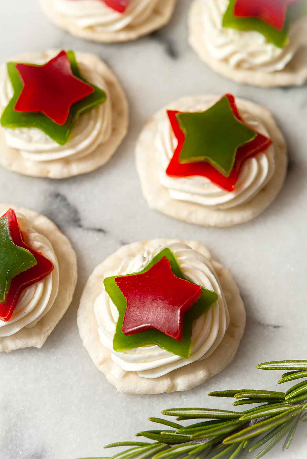 6 appetizers with stars made of bell pepper on marble beside a sprig of rosemary.