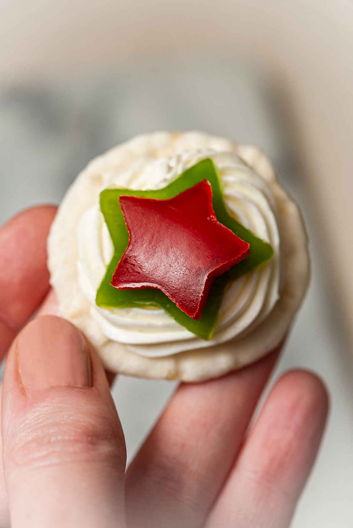 Fingers holding an appetizer with bell pepper stars and cream cheese.