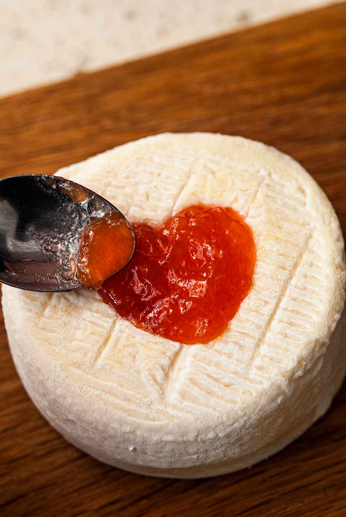 A spoon filling a cut-out heart on cheese with preserves.