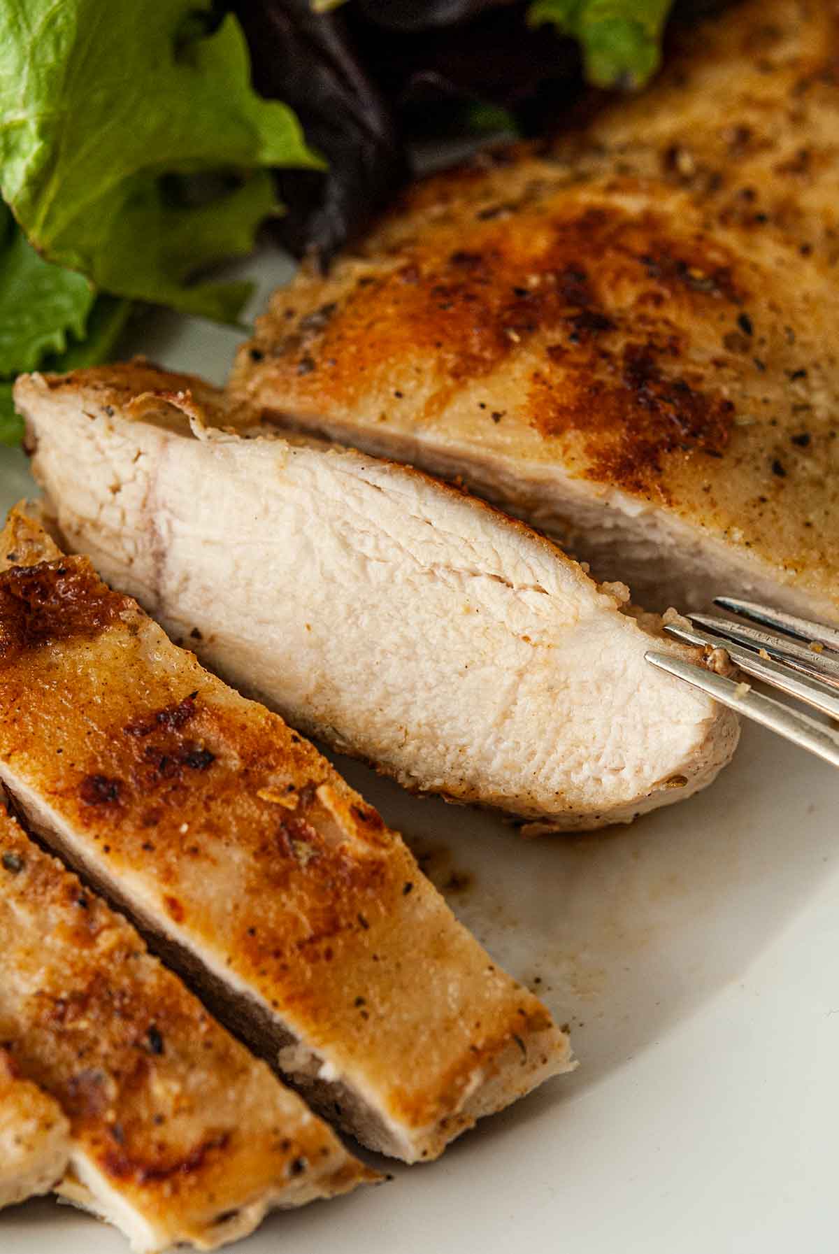 The juiciness of a sliced piece of chicken on a plate beside salad.