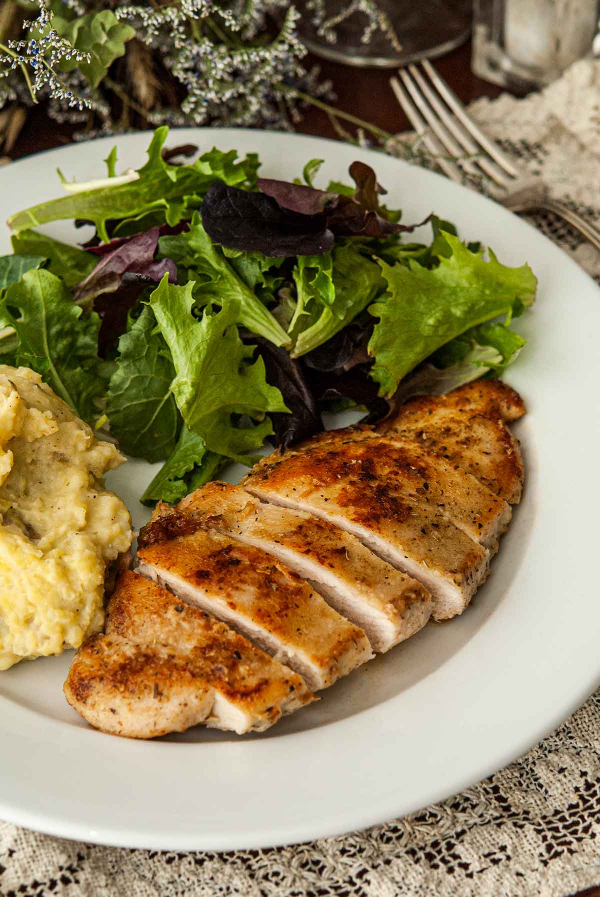 A sliced piece of chicken with Herbs de Provence on a plate with salad and potatoes.