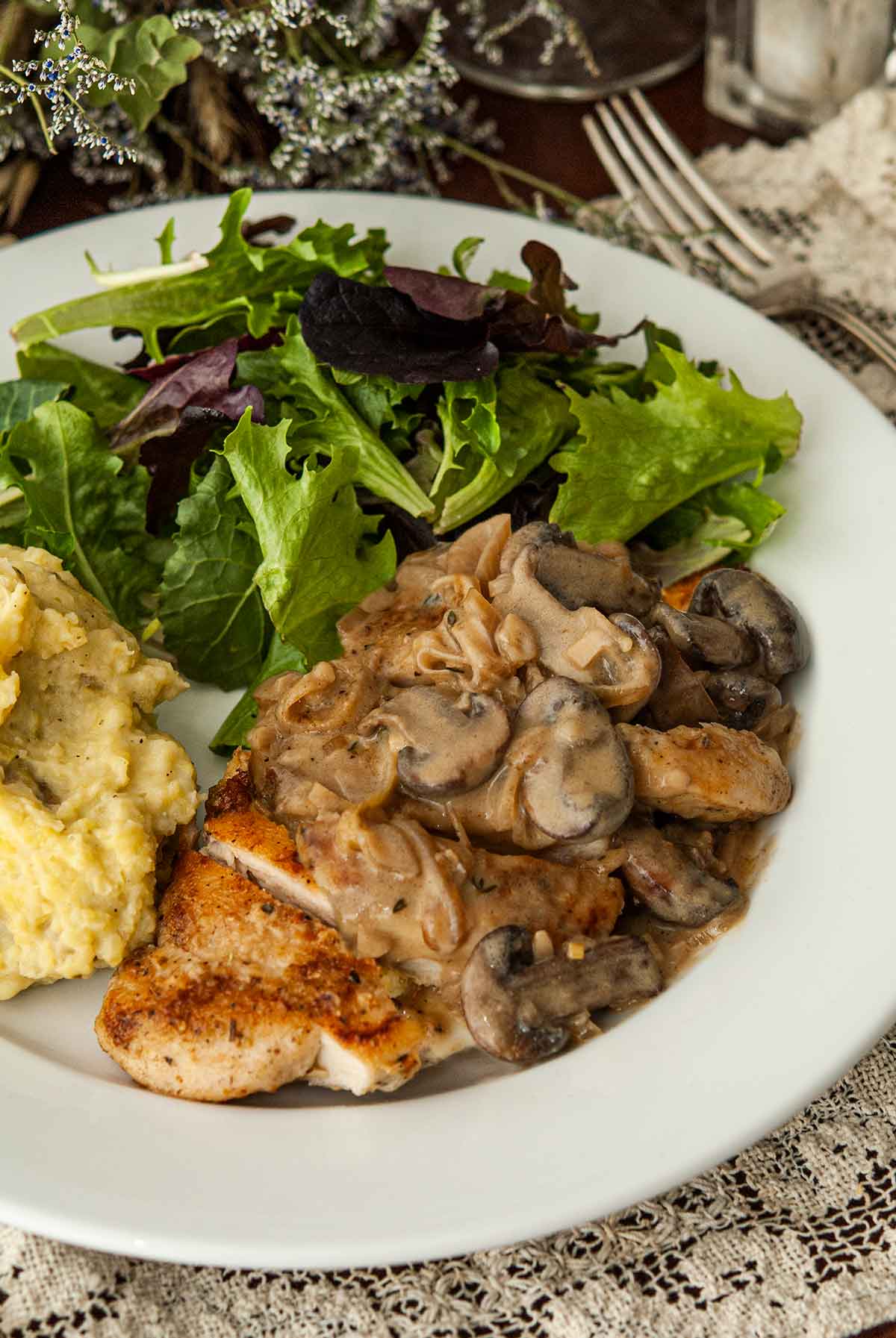 A sliced piece of chicken with Herbs de Provence and white wine mushroom sauce on a plate with salad and potatoes.