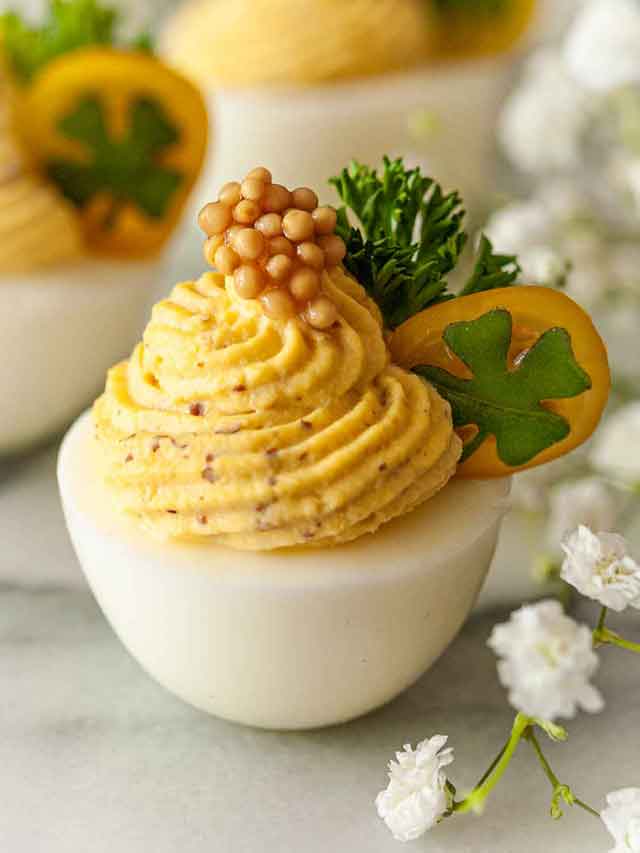 A deviled egg garnished with caviar, parsley and a clover on a tomato slice.