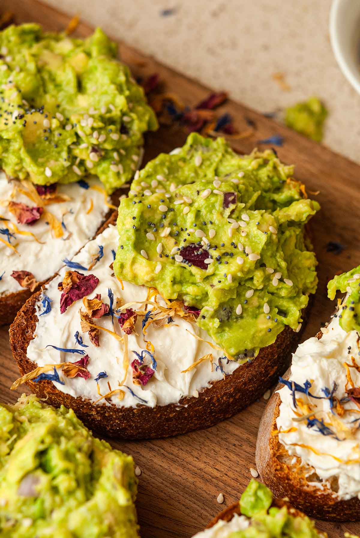 An avocado toast with flowers on a cutting board beside 4 others.