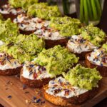 9 avocado toasts on a cutting board beside vases of daffodils.