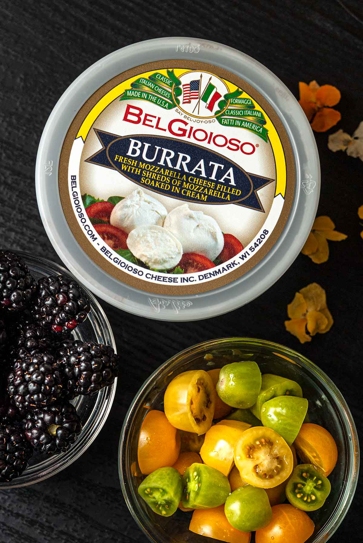 a Bel Gioioso burrata container on a table beside bowls of sliced tomatoes and blackberries.