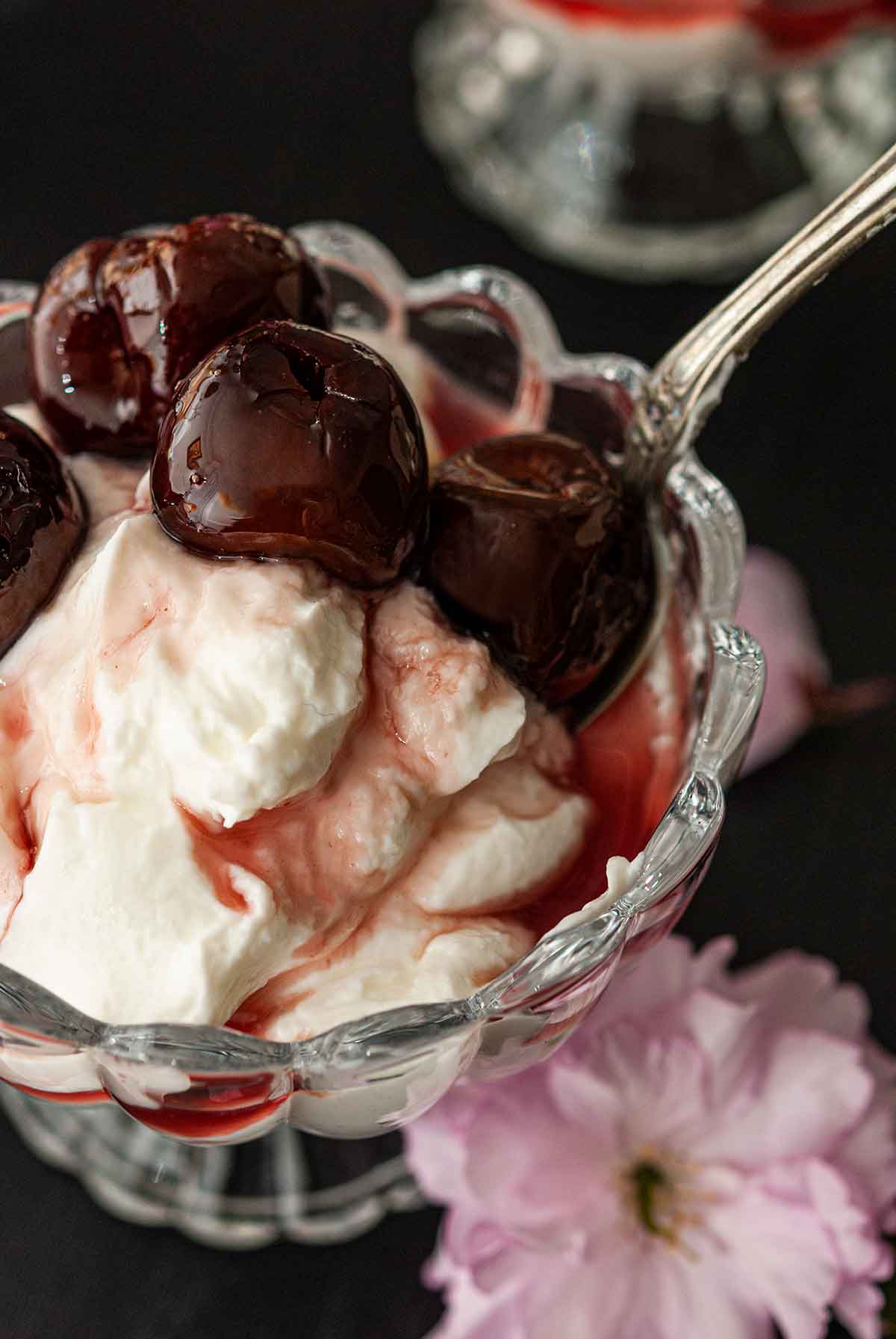 A spoon in a bowl of cherries and yogurt in a glass bowl.