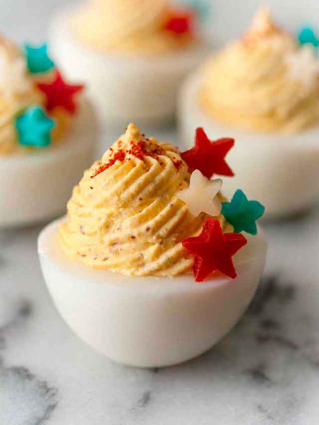 A deviled egg on marble, garnished with 4 stars made of red peppers and cheese that's both blue and white.