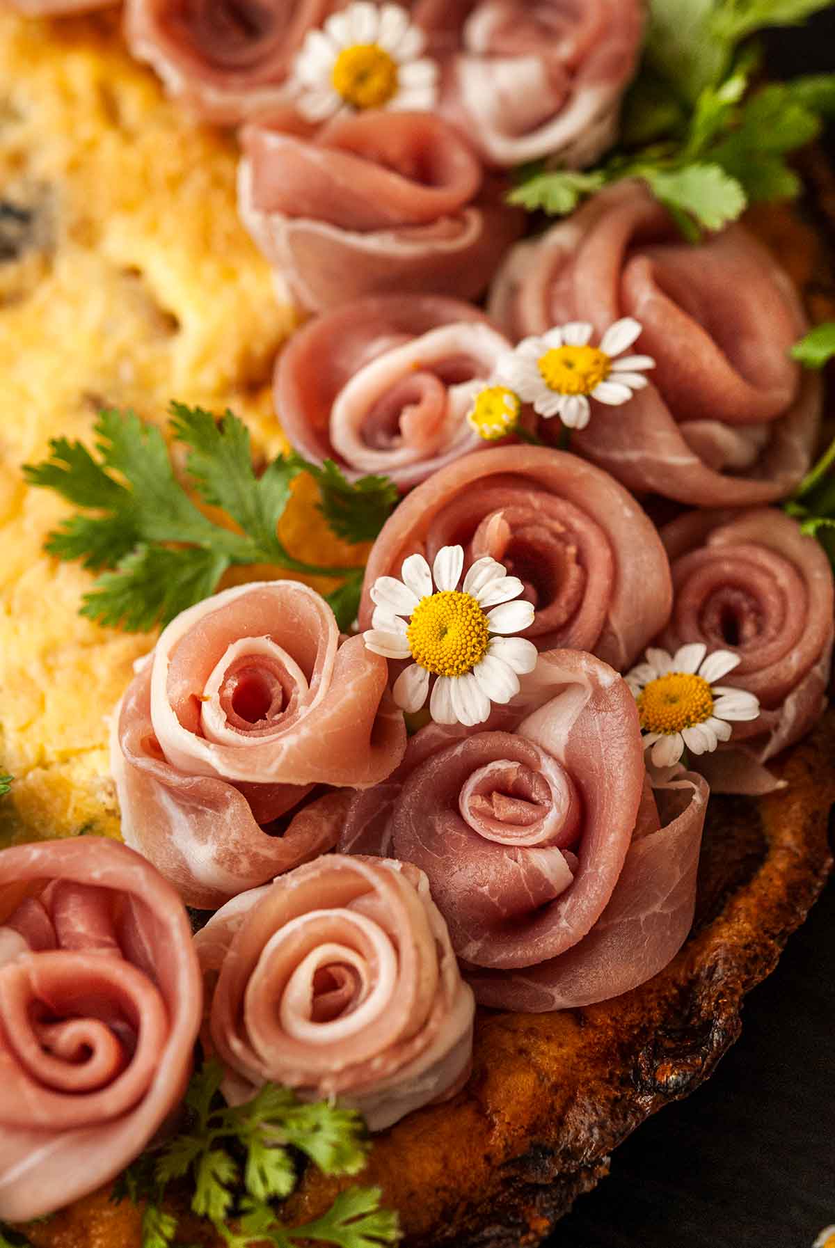 The prosciutto rose garnish on a quiche with flowers and parsley.