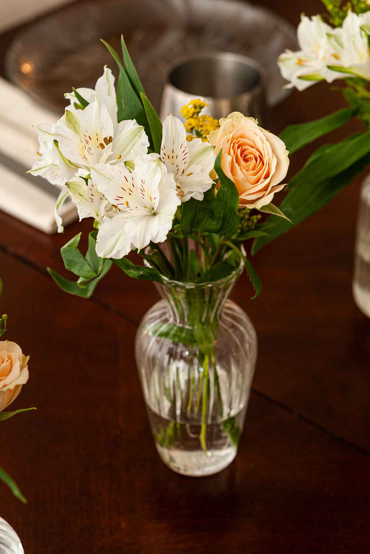 A small glass vase of flowers on a dining table.