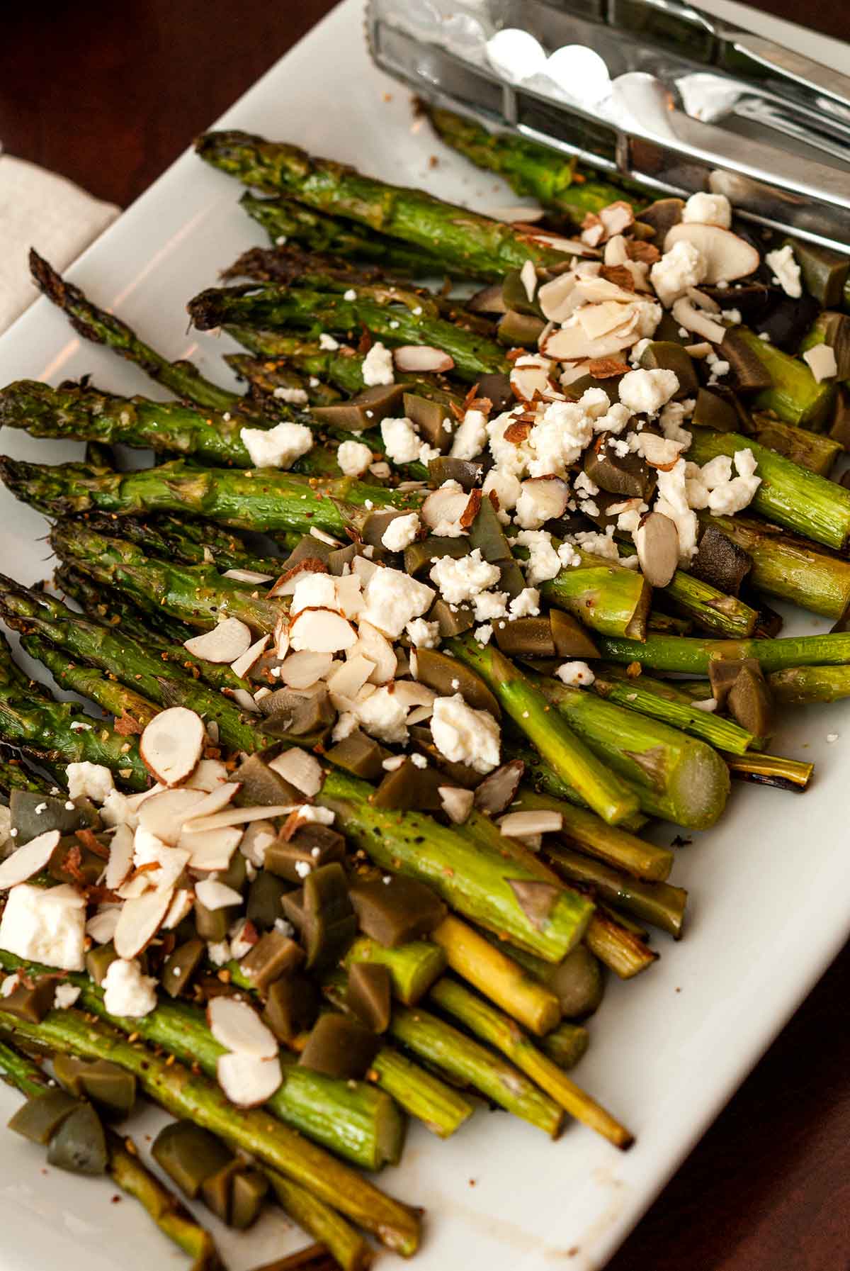 A plate of asparagus topped with feta, almonds and olives.
