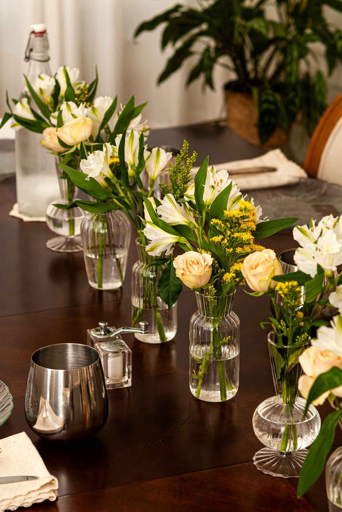 A dining room table with 6 vases of flowers.