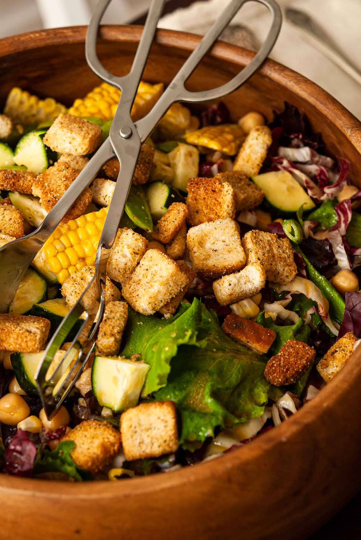 A wooden bowl of salad with salad tongs.