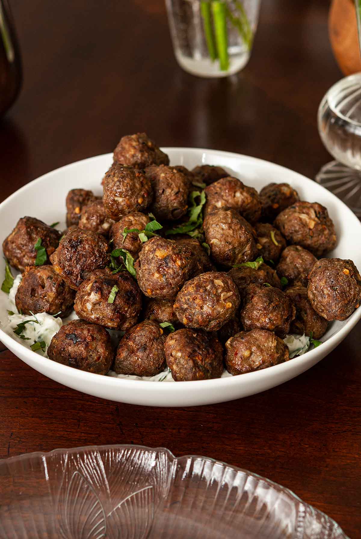 A bowl of meatballs with tzatziki on a table.