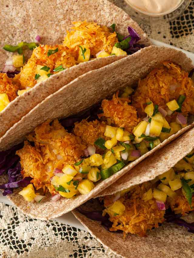 3 coconut shrimp tacos topped with pineapple jalapeño salsa on a table.