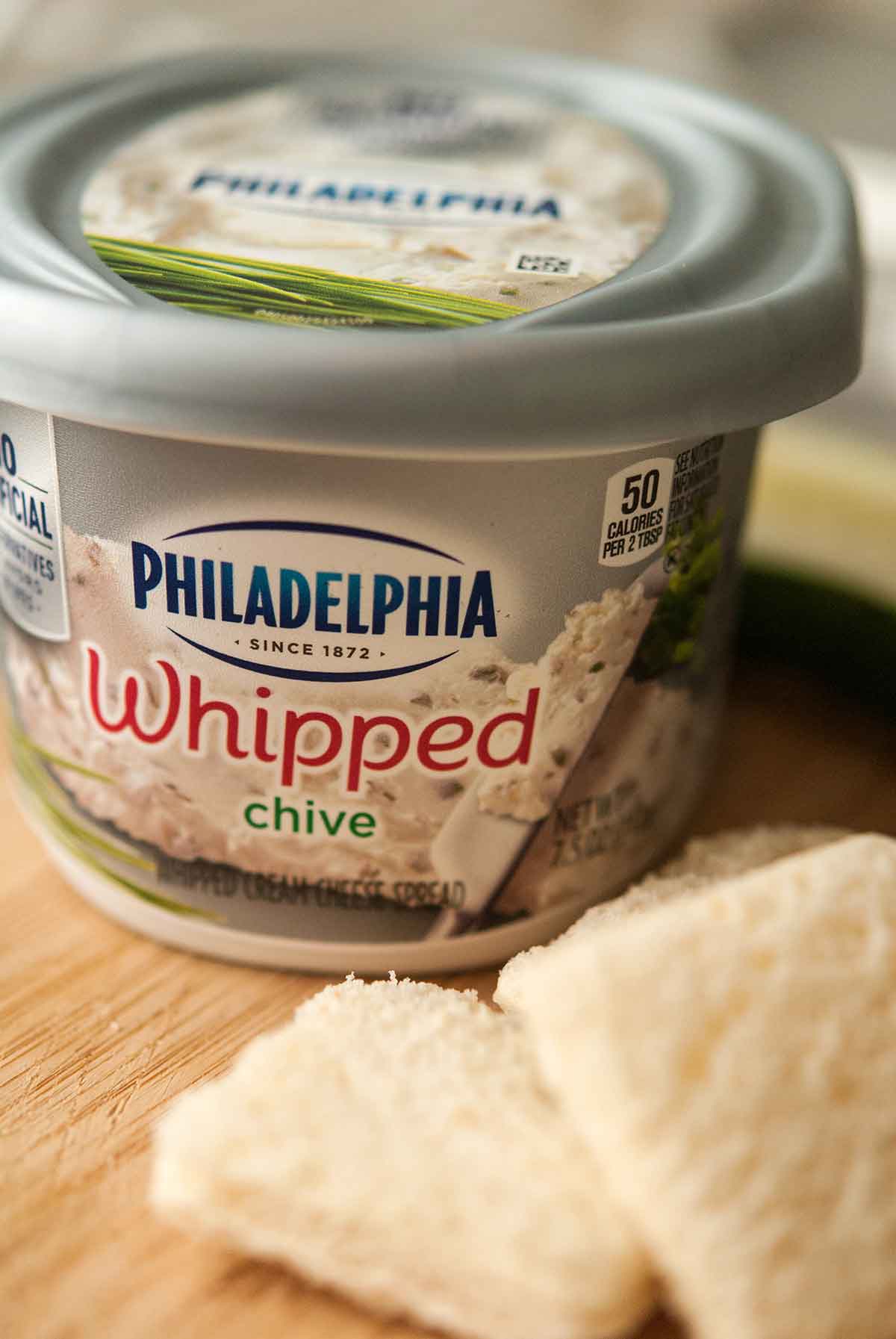 A container of Philadelphia whipped cream cheese beside 2 slices of bread.