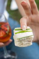 A finger holding a cucumber sandwich.