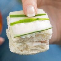 A finger holding a cucumber sandwich.