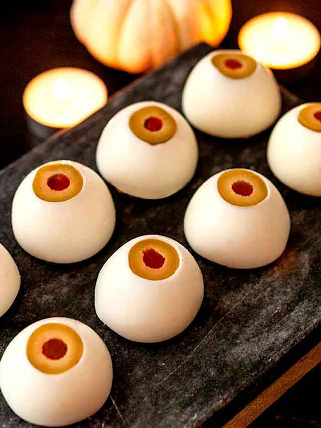 8 deviled eyeballs on a slate, in front of a small pumpkin and candles.