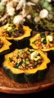 4 acorn squash on a wooden plate in front of dry flowers on a table.