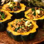 4 stuffed acorn squash garnished with a flower and thyme on a wooden plate.