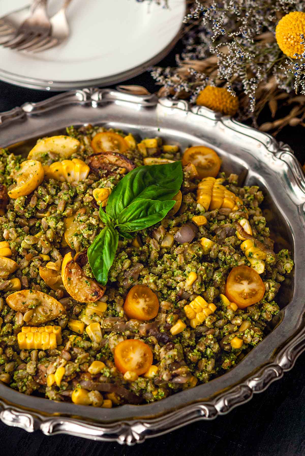 A decorative silver bowl full of pesto farro with plates in the background.