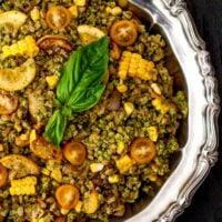 A silver bowl full of pesto farro with assorted vegetables.