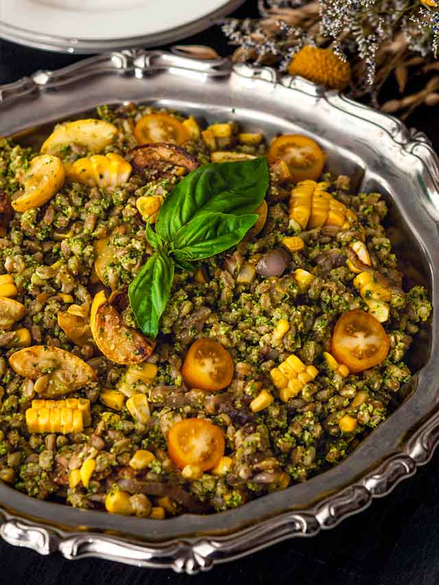 A silver bowl on a table full of pesto farro with assorted vegetables.