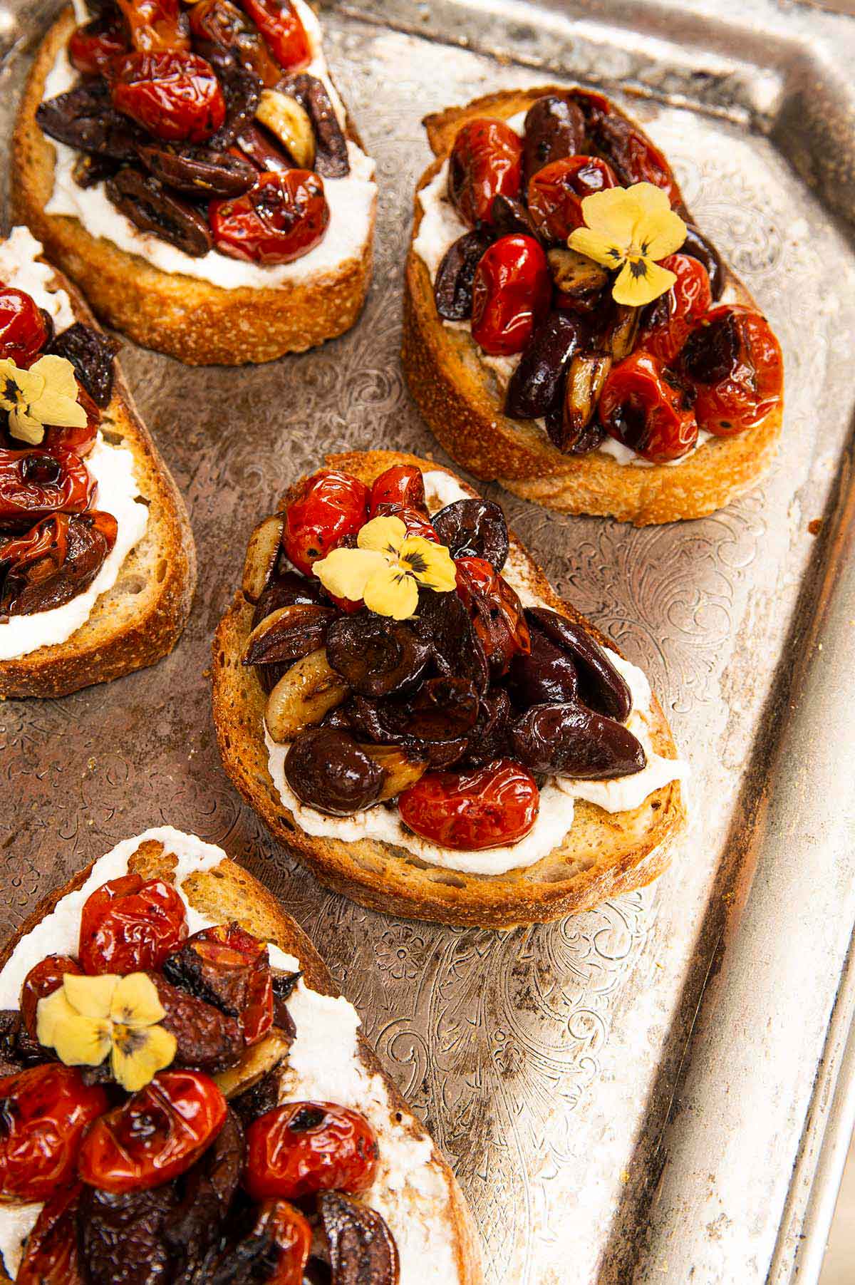 5 tomato bruschetta on a silver platter, garnished with flowers.