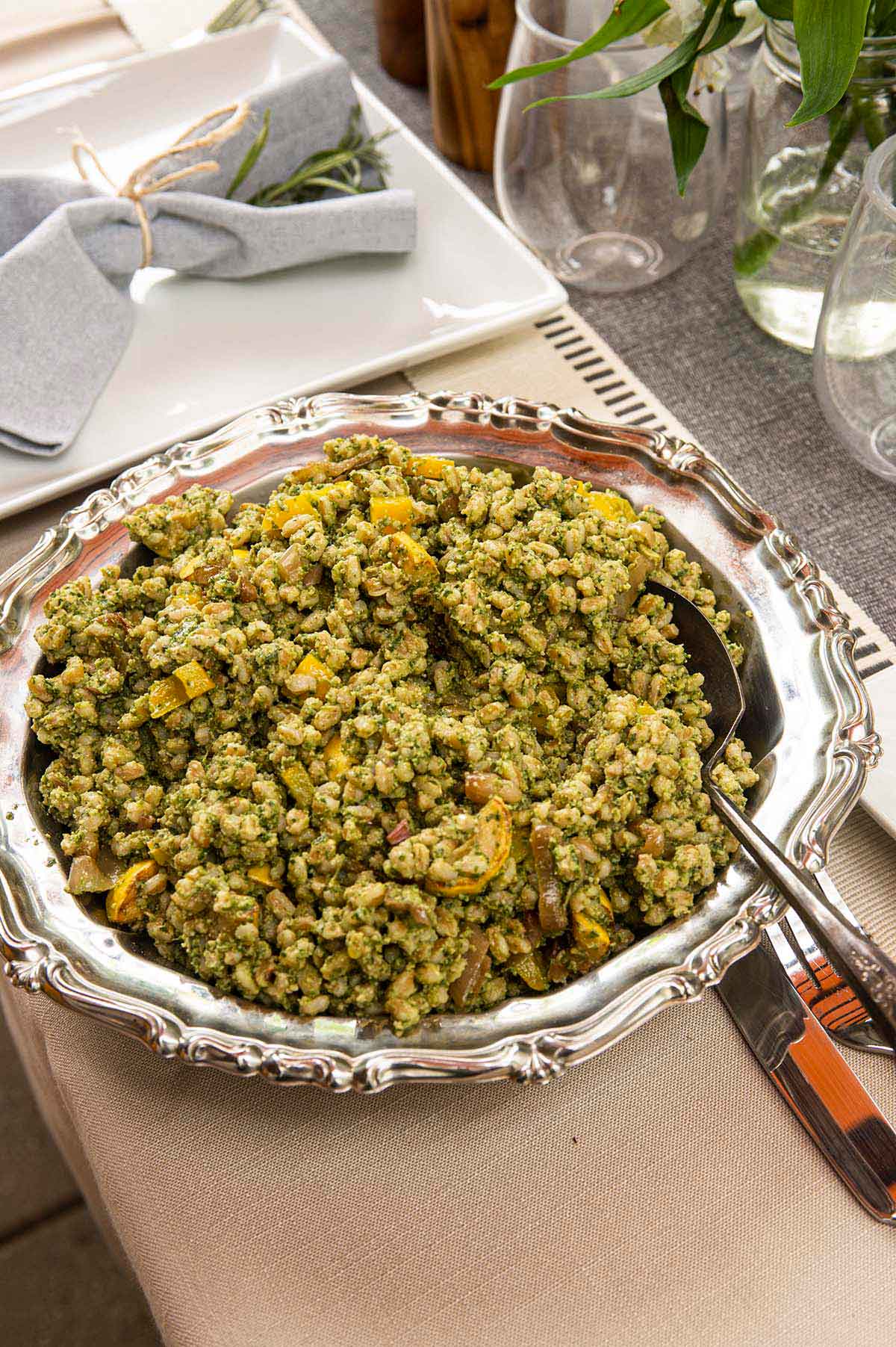 A decorative silver bowl with pesto farro on a set table.