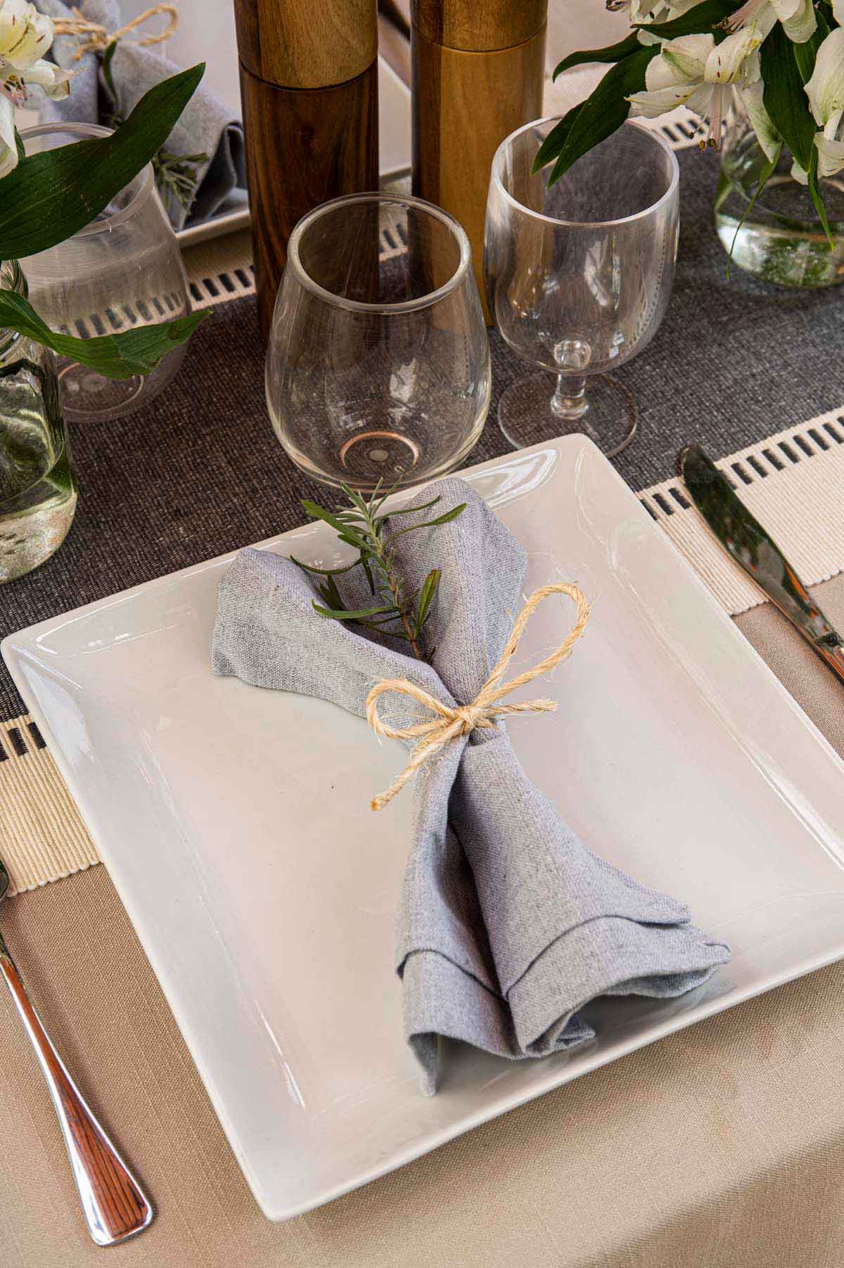 A napkin with a sprig of lavender greens tied to it on a plate on a table.