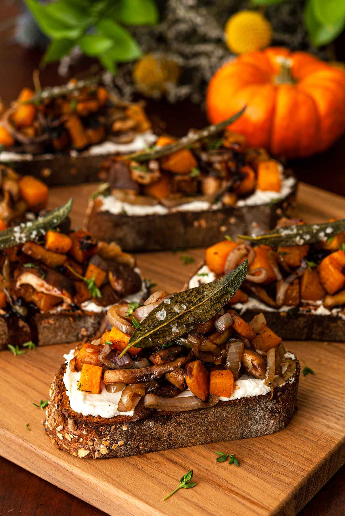 5 maple butternut squash crostini on a board in front of a pumpkin and greenery.