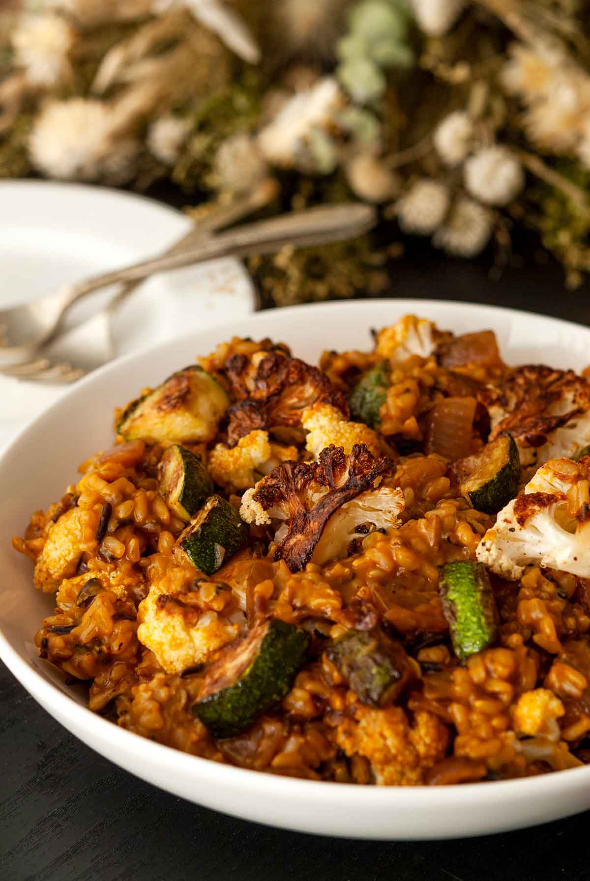 A bowl of pumpkin rice with fall vegetables on a table with dry flowers and plates.