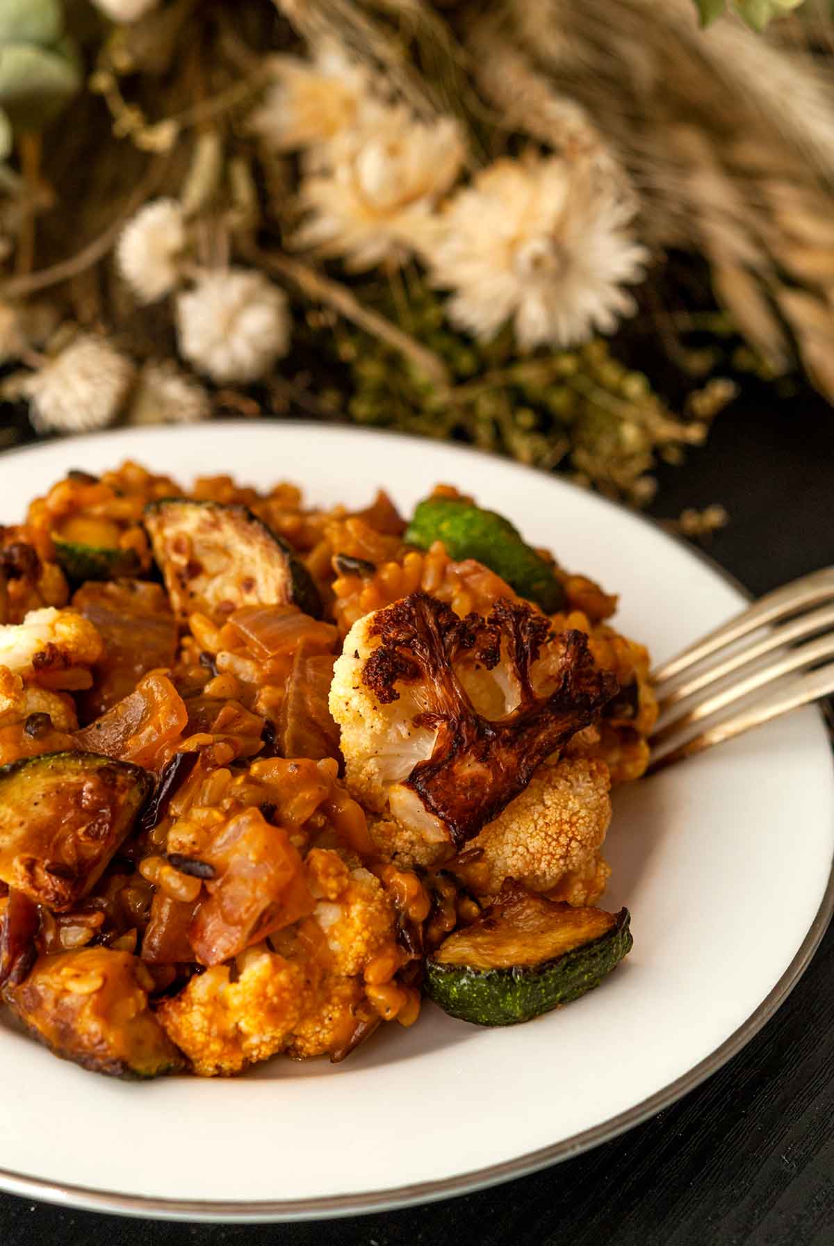 A plate of pumpkin rice with fall vegetables on a table with dry flowers.