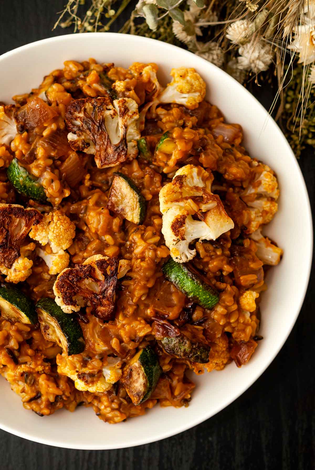 A bowl of pumpkin rice with fall vegetables on a table with dry flowers.