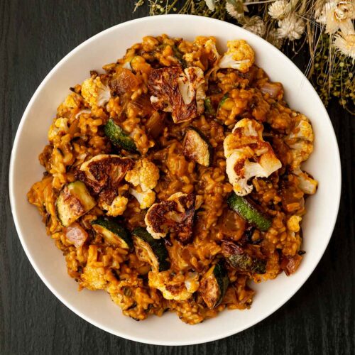 A centered bowl of pumpkin rice with fall vegetables on a table with dry flowers.