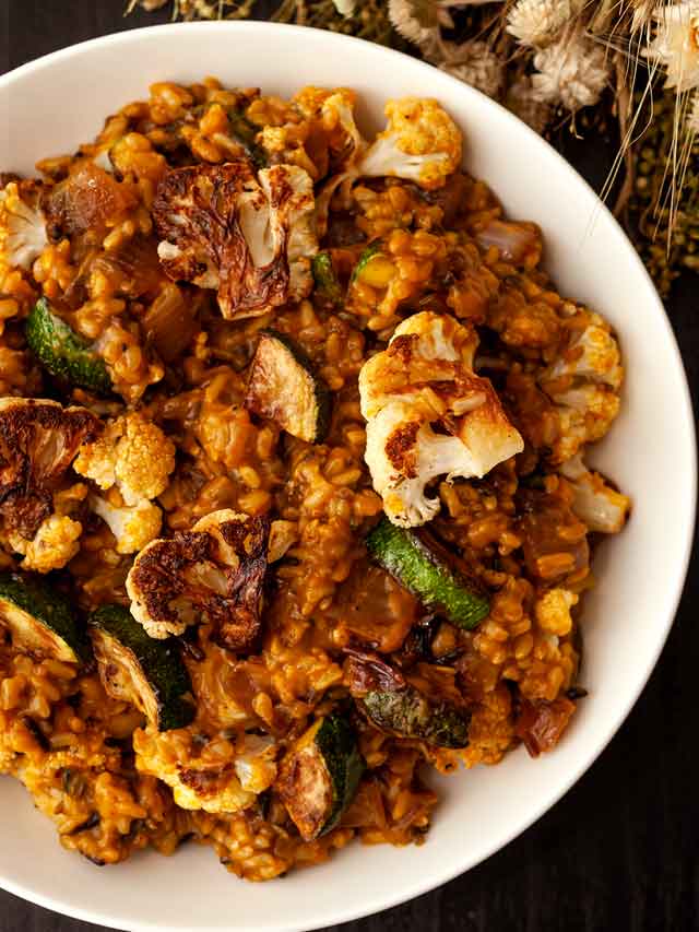 A bowl of pumpkin rice with fall vegetables on a table with dry flowers.