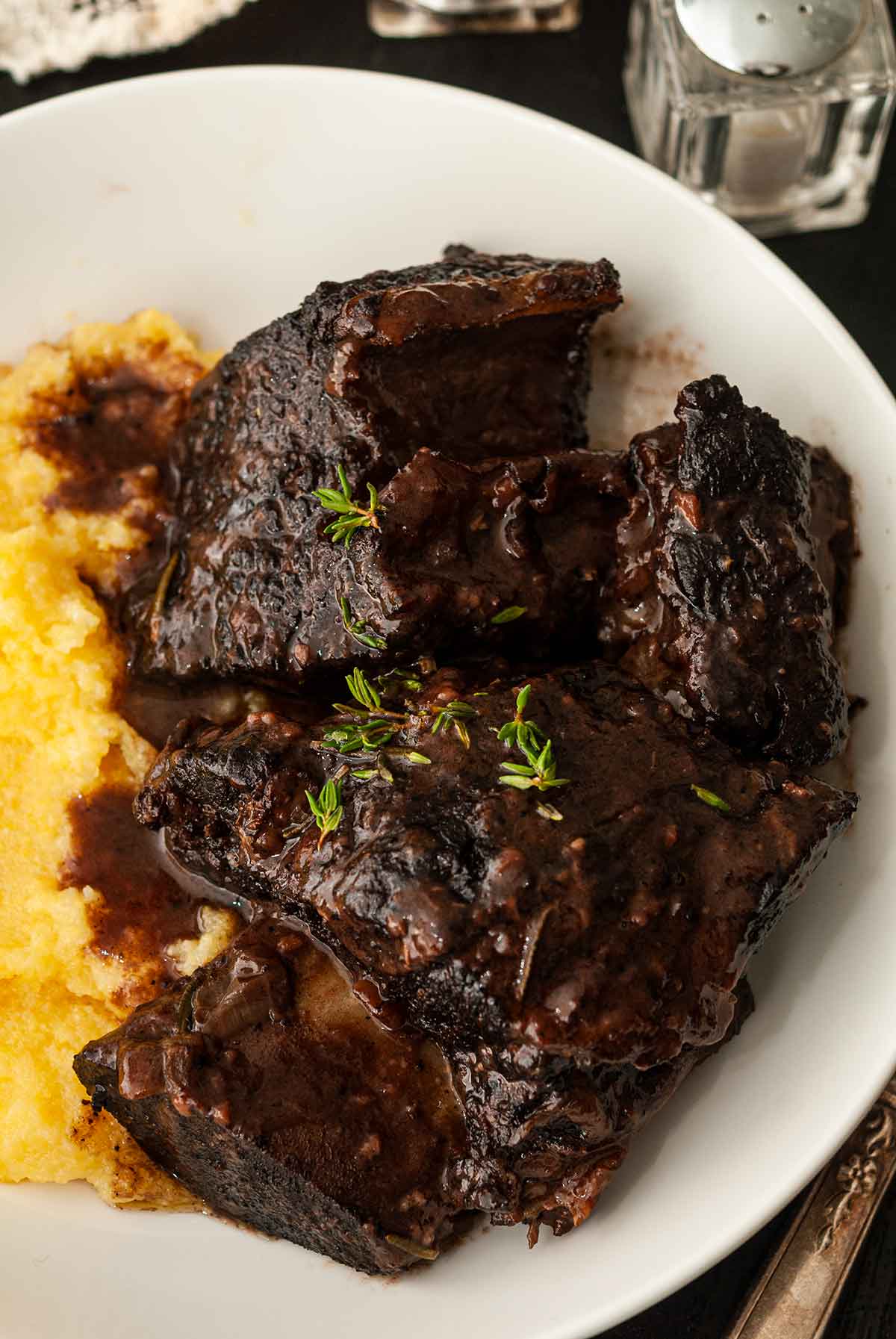 The meat of braised short ribs in a bowl with polenta, garnished with thyme.