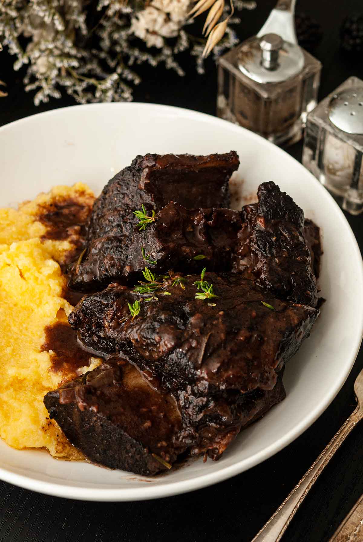 Braised short ribs in a bowl with polenta, garnished with thyme.