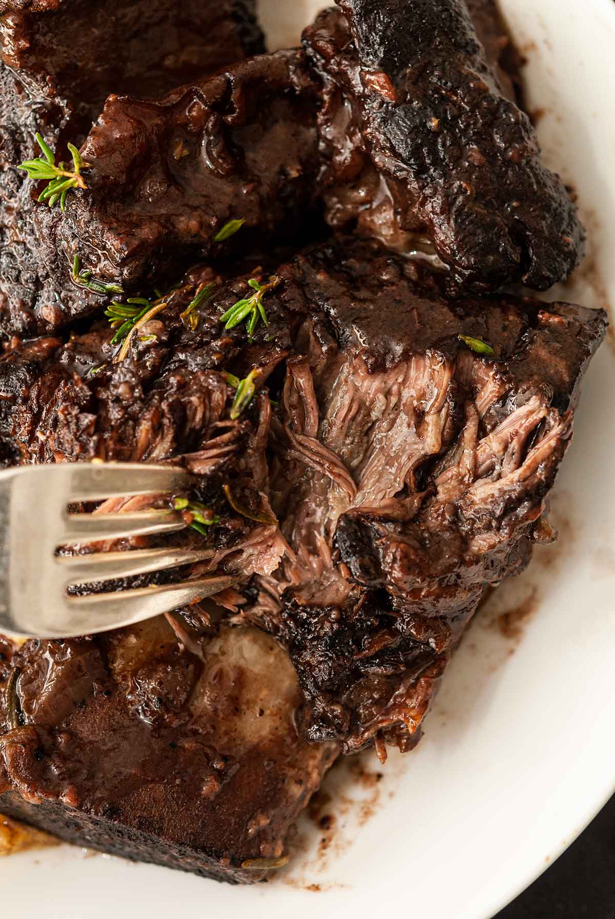 A fork pulling apart the meat of a braised short rib.