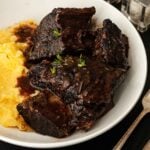 Braised short ribs in a bowl with polenta, garnished with thyme.