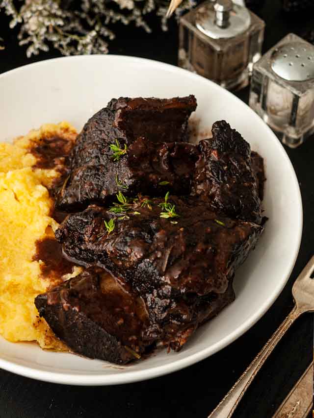 Braised short ribs in a bowl with polenta, garnished with thyme.