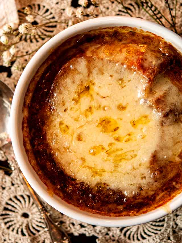 A bowl of French onion soup on a small lace doily.