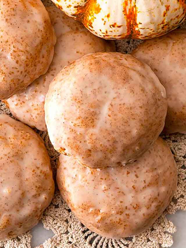 7 glazed cookies on lace, beside a pumpkin gourd.