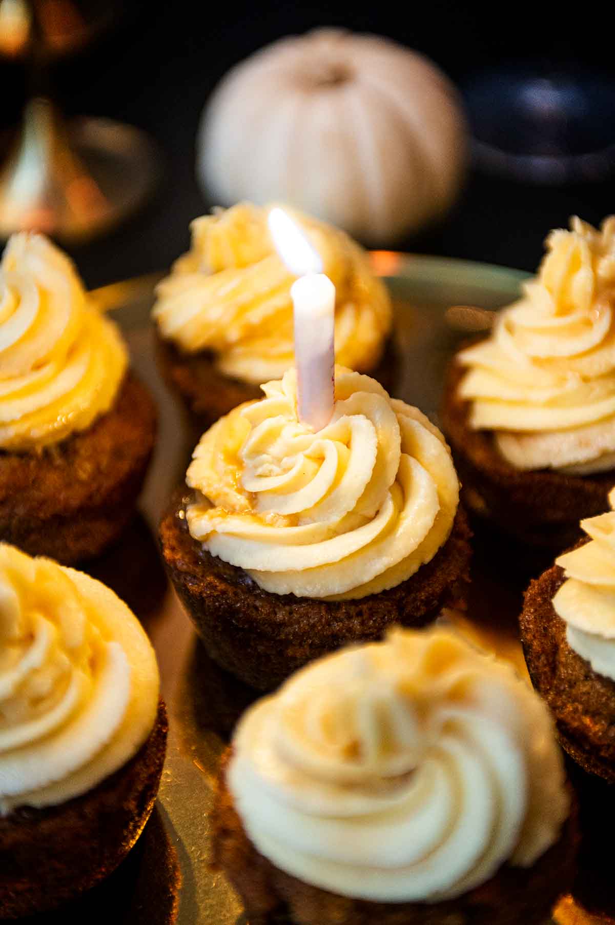 7 cupcakes with on a tray, the center having a lit birthday candle.