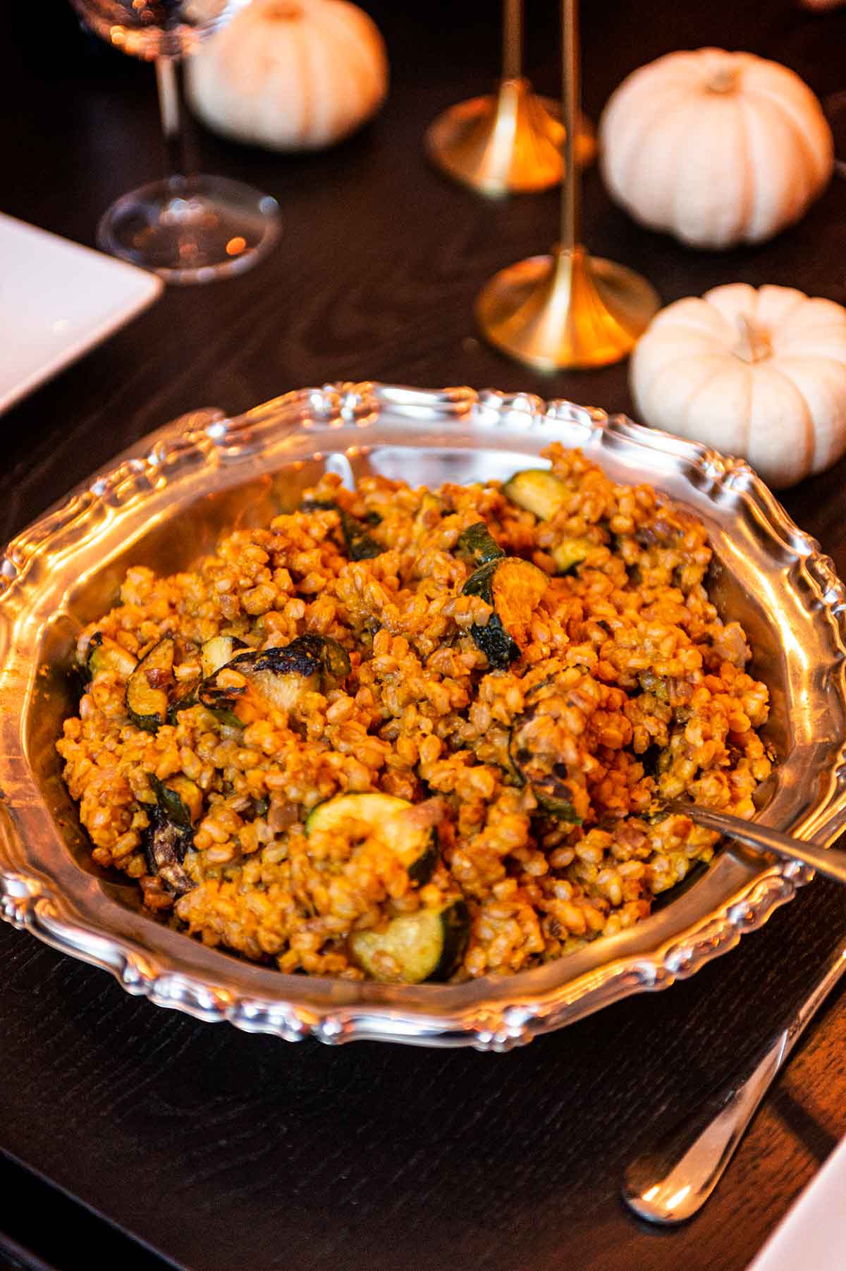 A metal bowl of pumpkin farro on a table beside white pumpkins.