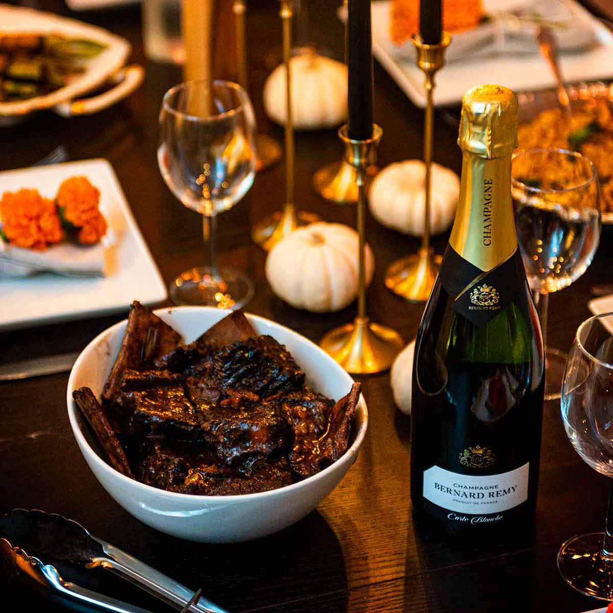 A dark dinner table with black candles, marigolds, short ribs and champagne.