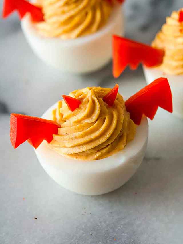 A deviled egg with bell pepper horns and wings on a marble plate with 2 others in the background.