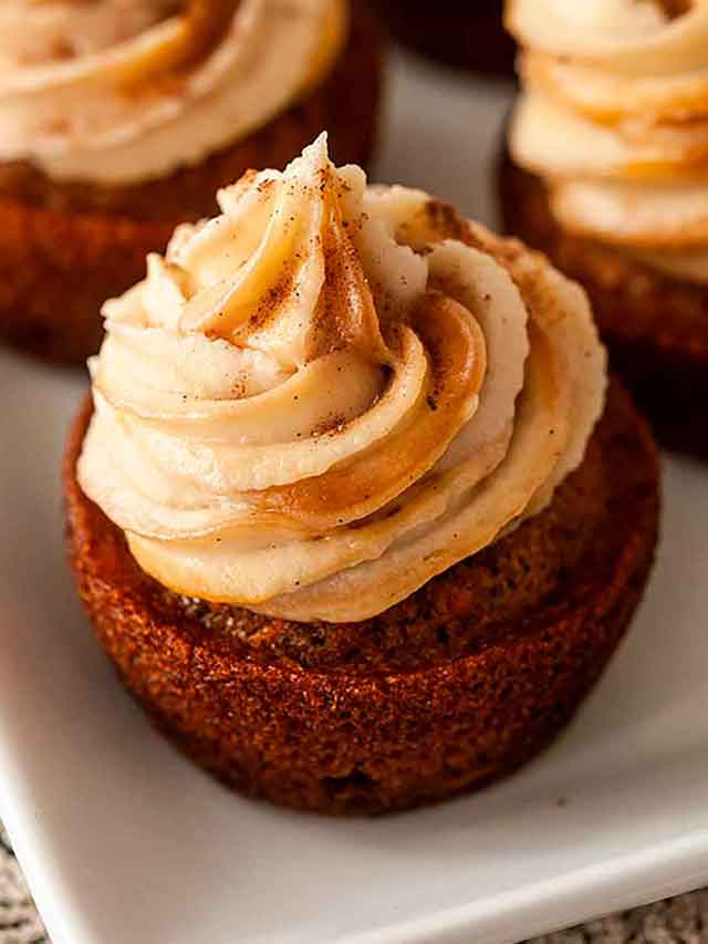 A frosted cupcake on a plate beside 3 others.